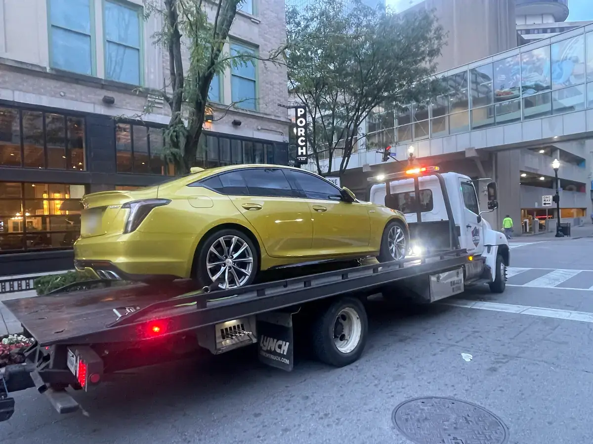 Joe Towing flatbed carrying a yellow sedan on a city street.