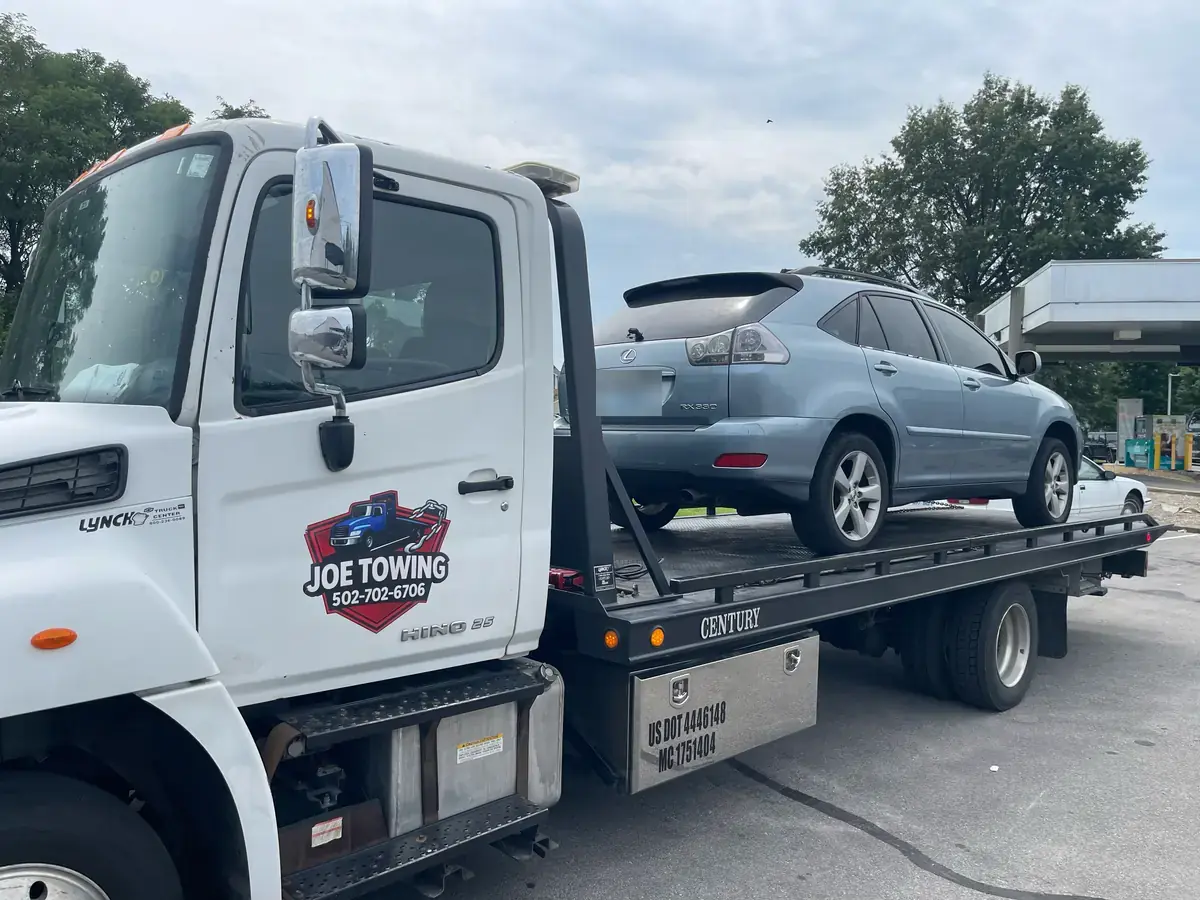 Joe Towing truck door with the logo and the number 502-702-6706, an SUV loaded on the flatbed.